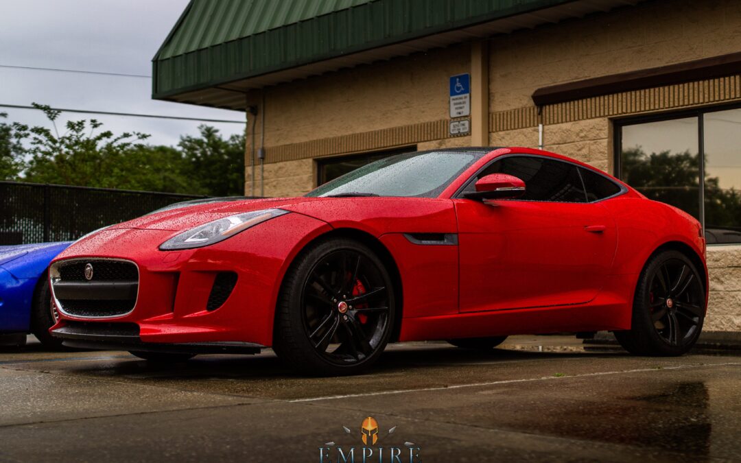 Red Jaguar F-TYPE parked in front of a building. The car has a ceramic coating, which gives it a shiny and durable finish. The coating also helps to protect the car from scratches, dents, and UV rays. The logo of Empire Auto Spa, a Central Florida car detailing and ceramic coating company, can be seen on the building.