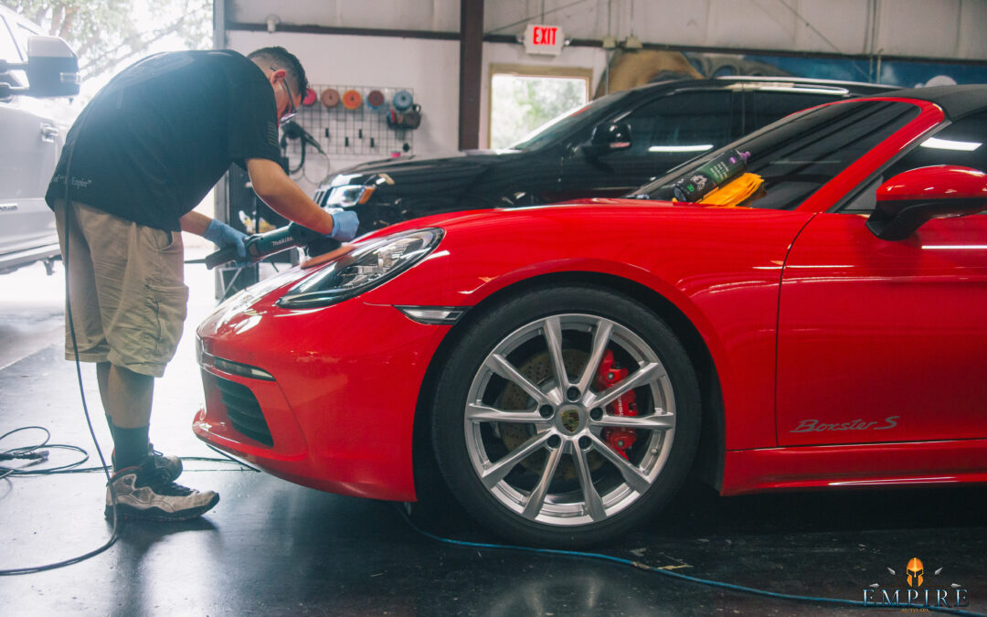 A man is polishing a red sports car in a garage. The car has a custom paint job, body kit, and wheels.