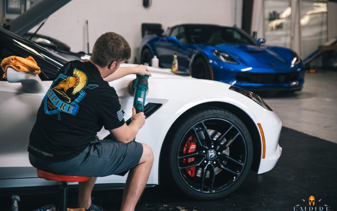 Image of a man applying ceramic coating for cars to a car wheel at Empire Auto Spa. The man is wearing gloves and safety glasses, and he is using a spray bottle to apply the coating. The wheel is a shiny silver color.