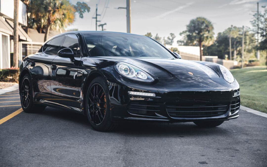 A black Porsche Panamera 4 parked in a parking lot. The car has a few swirl marks and scratches on the paintwork.