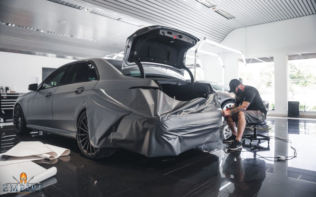 Professional at Empire Auto Spa meticulously applying a vinyl wrap, showcasing the transformation and detailing expertise.