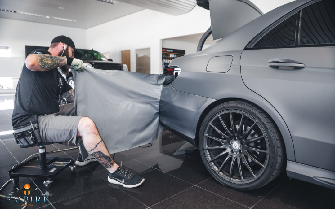 Empire Auto Spa technician expertly applying vinyl wrap on a car, showcasing the professional car wrapping process.