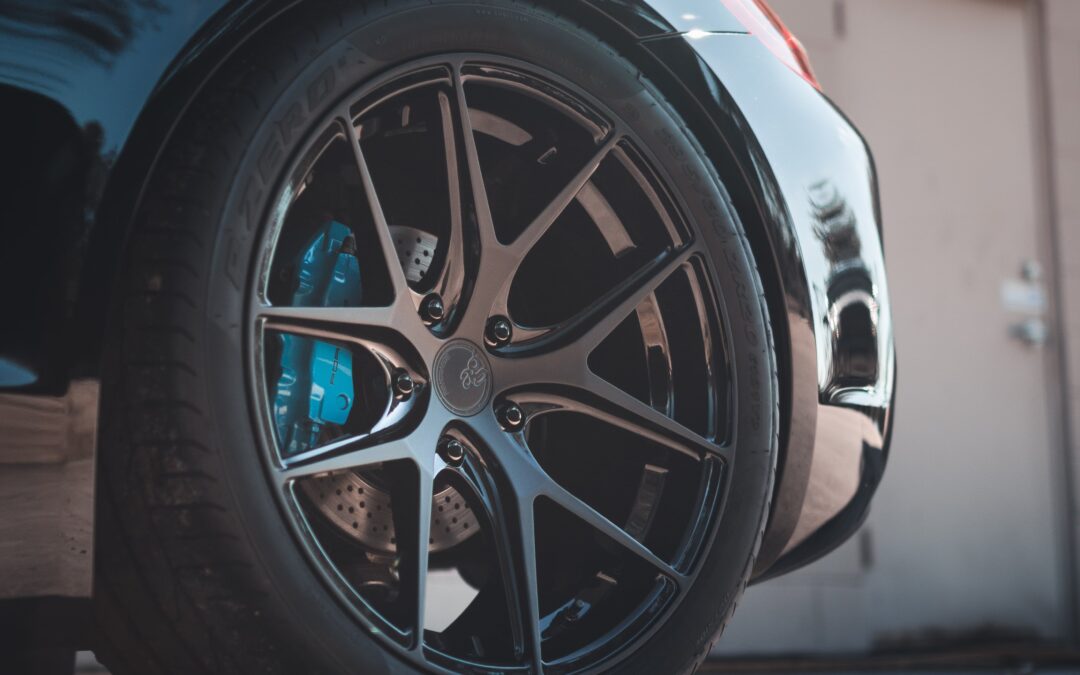 Close-up of a Porsche Taycan wheel. The wheel is made of silver metal and has five spokes. The center of the wheel has the Porsche logo.